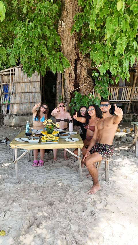 A small group enjoying an outdoor meal at a rustic beach hut table.