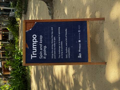A wooden signboard explaining a Filipino spinning-top game set on a sandy pathway.