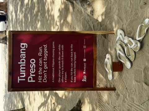 Instructional sign about a traditional Filipino chasing game with slippers placed beside it.