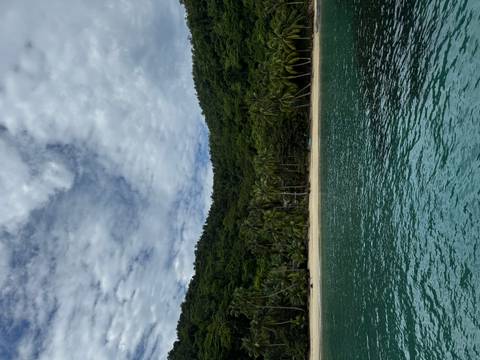 Turquoise water in front of a secluded tropical beach backed by lush green hills and palms.