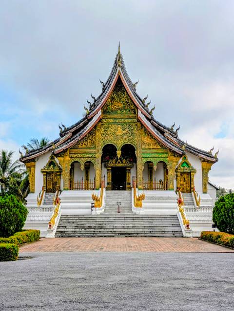 Ornate gilded Buddhist temple facade with white staircases and naga statues under a soft sky