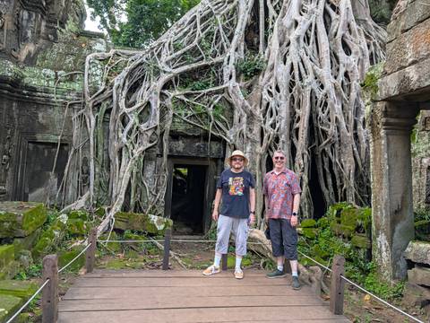 Two travellers posing in front of massive strangler-fig roots engulfing an ancient stone doorway