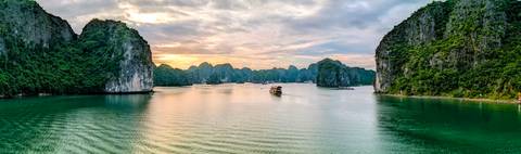 Scenic panorama of emerald water and limestone peaks of Ha Long Bay at golden sunset