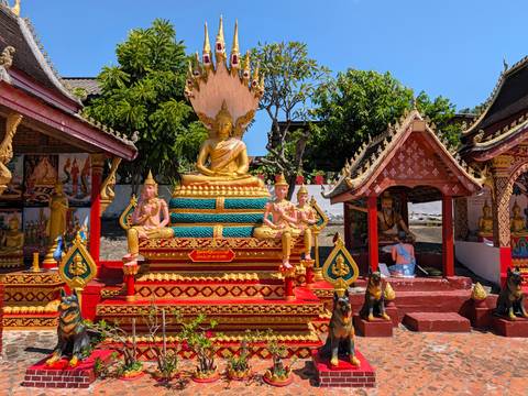 Brightly painted outdoor Buddhist shrine with golden seated Buddha against blue sky