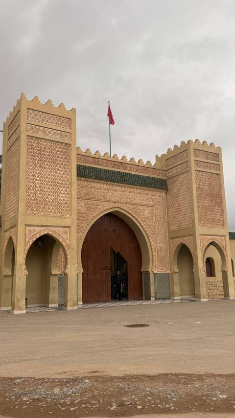 An ornate Moroccan city gate with intricate geometric carvings and pointed arches under an overcast sky.