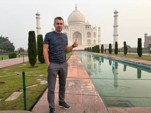 Traveler gives thumbs-up beside reflecting pool leading to the Taj Mahal at dawn haze.