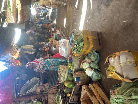 A vendor stands beside colourful baskets of produce inside a busy local market.