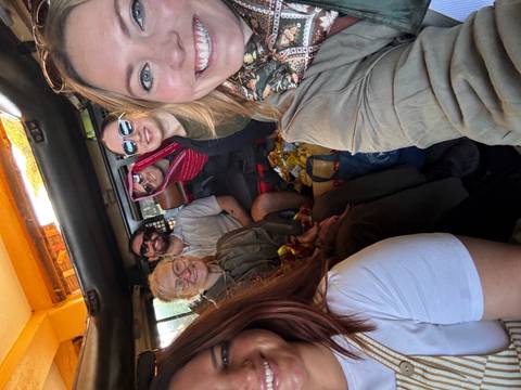 Smiling travelers take a selfie inside a safari vehicle packed with gear.