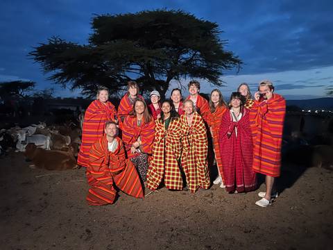 Large group draped in red Maasai shukas poses with livestock under a twilight sky.