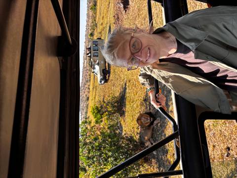 Traveler inside a safari jeep smiles with a resting male lion visible through the window behind.