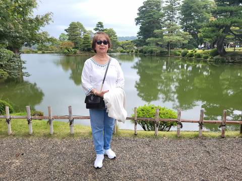 Woman poses beside a reflective pond and manicured trees in Kanazawa’s Kenrokuen Garden.