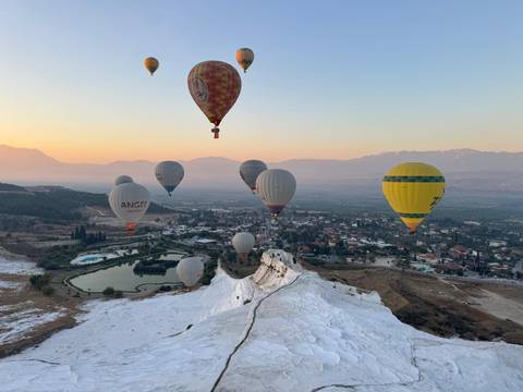 Dozens of hot-air balloons soar over Pamukkale’s white travertine terraces at sunrise.