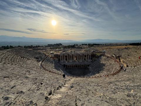 The sun sets over the vast stone amphitheater of Hierapolis with long shadows across the seats.