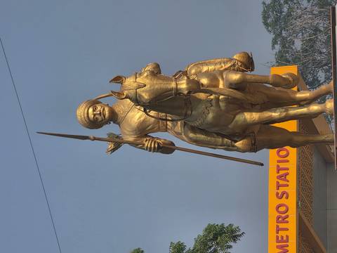 A towering golden equestrian statue stands outside a metro station against a clear sky.