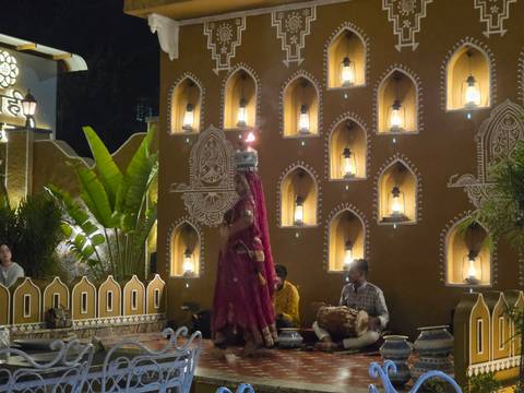 A traditional Rajasthani dancer balances pots on her head while musicians play in a lantern-lit courtyard.