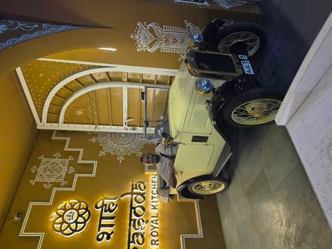 A smiling man poses in a vintage open-top car inside a stylishly decorated restaurant entrance.
