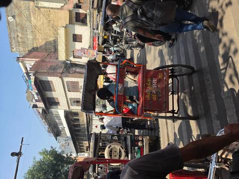 A cycle rickshaw navigates a busy street lined with shops and traffic in an Indian city.