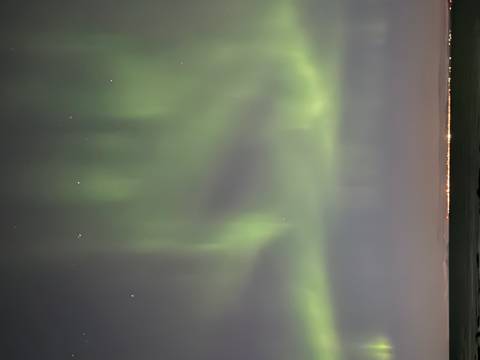 Green aurora borealis lights dancing in the night sky above a distant coastline.