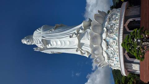 Towering white Lady Buddha statue atop a lotus pedestal under a clear blue sky