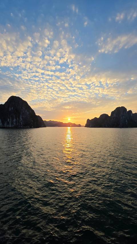 Halong Bay sunset with golden light reflecting on calm emerald waters between karst islands