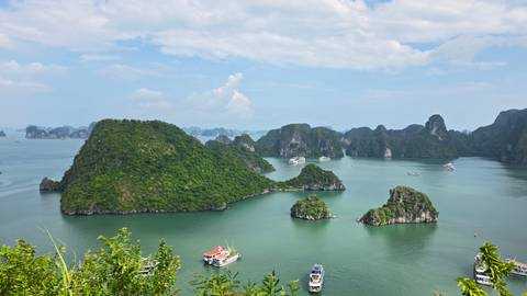 High viewpoint over green limestone islands and boats dotting turquoise Halong Bay