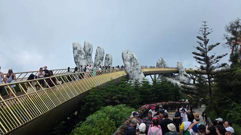 Crowds of tourists walk along the Golden Bridge’s curving span supported by giant hands