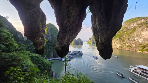 View from inside a cave opening onto limestone cliffs and cruise boats in Halong Bay