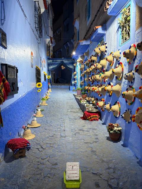 Narrow alley in Chefchaouen painted vivid blue, lined with colourful woven hats and sunflowers
