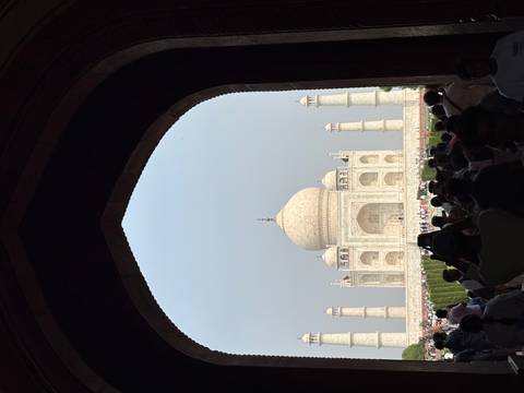 Iconic Taj Mahal framed by a dark archway with crowds of visitors in the foreground.