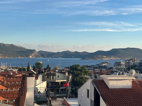 Panoramic coastal town with tiled rooftops, marina and surrounding hills.
