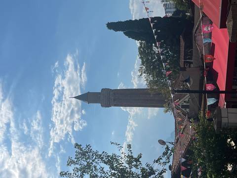 Tall brick minaret rises above rooftops and festive bunting under a blue sky.