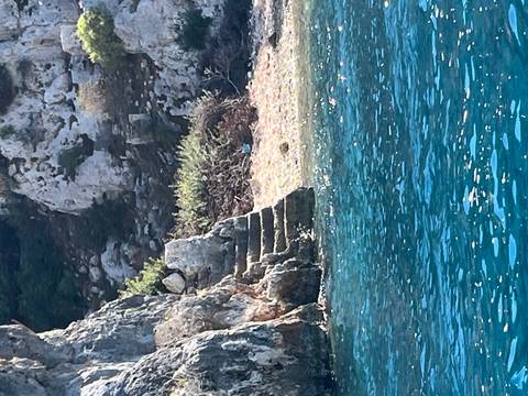 Stone steps carved into a rocky shoreline descend into clear blue water.