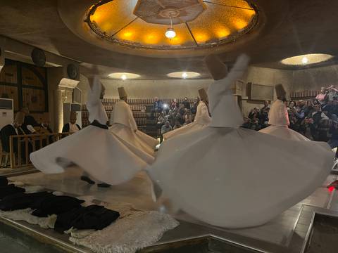 Whirling dervishes in flowing white robes spin in a softly lit cultural performance hall.