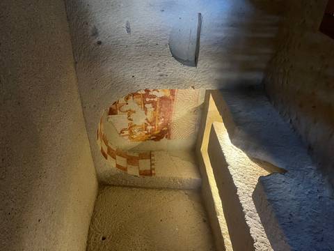 Interior of a rock-cut chapel with faded frescoes and hewn stone benches.