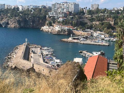 Clifftop view of a harbor with boats, breakwater and deep blue sea below.