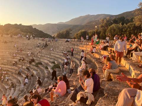 Ancient amphitheatre bathed in warm evening light, filled with spectators on stone tiers.