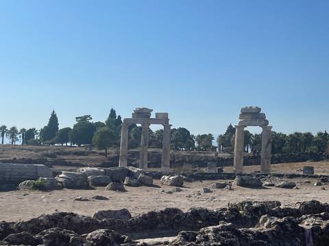 Four standing stone columns amid scattered ruins under a clear blue sky.