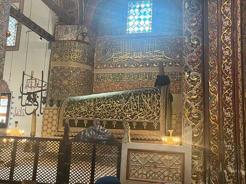 Ornately decorated tomb covered in intricate Arabic calligraphy inside a dimly lit shrine.