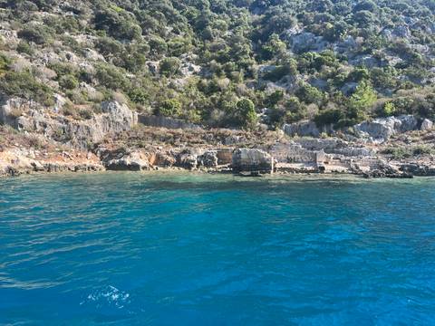 Rocky coastline with clear blue water and sparse ancient stone remains at the shore.