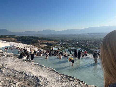 Crowds wading through thermal pools on the white terraces of Pamukkale with a valley view beyond.