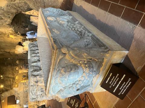 Ancient sarcophagus with detailed relief carvings displayed in a museum with visitors nearby.