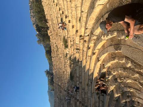 Visitor sitting on the stone steps of an ancient theatre under clear blue skies.