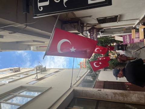 Narrow alley adorned with multiple Turkish flags fluttering overhead between tall buildings.