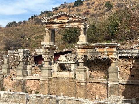 Partially reconstructed Roman nymphaeum with columns and architrave set against a hillside.