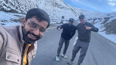 Selfie of three friends on a snowy mountain road smiling and gesturing cheerfully.