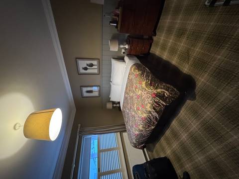 Cozy hotel bedroom with patterned duvet, plaid carpet and warm lamp lighting.