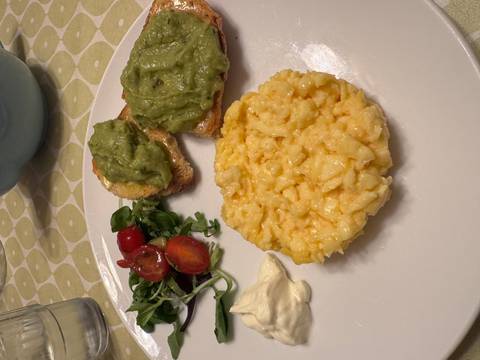 Breakfast plate featuring creamy scrambled eggs, avocado toast, salad greens and tomatoes.