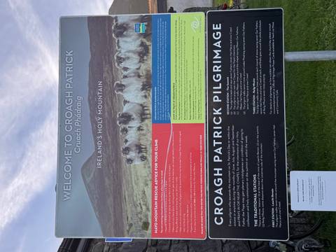 Visitor information board welcoming climbers to Croagh Patrick, set against grassy hillside.