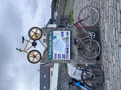 Outdoor stone plinth holding a bicycle and a detailed tourist map of Inis Oírr island with photos.
