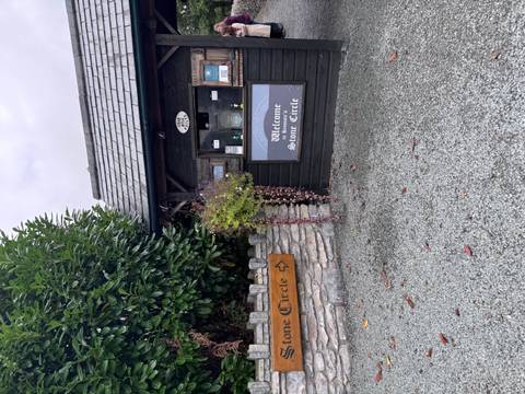 Small wooden kiosk and sign welcoming visitors to Kenmare Stone Circle surrounded by greenery.